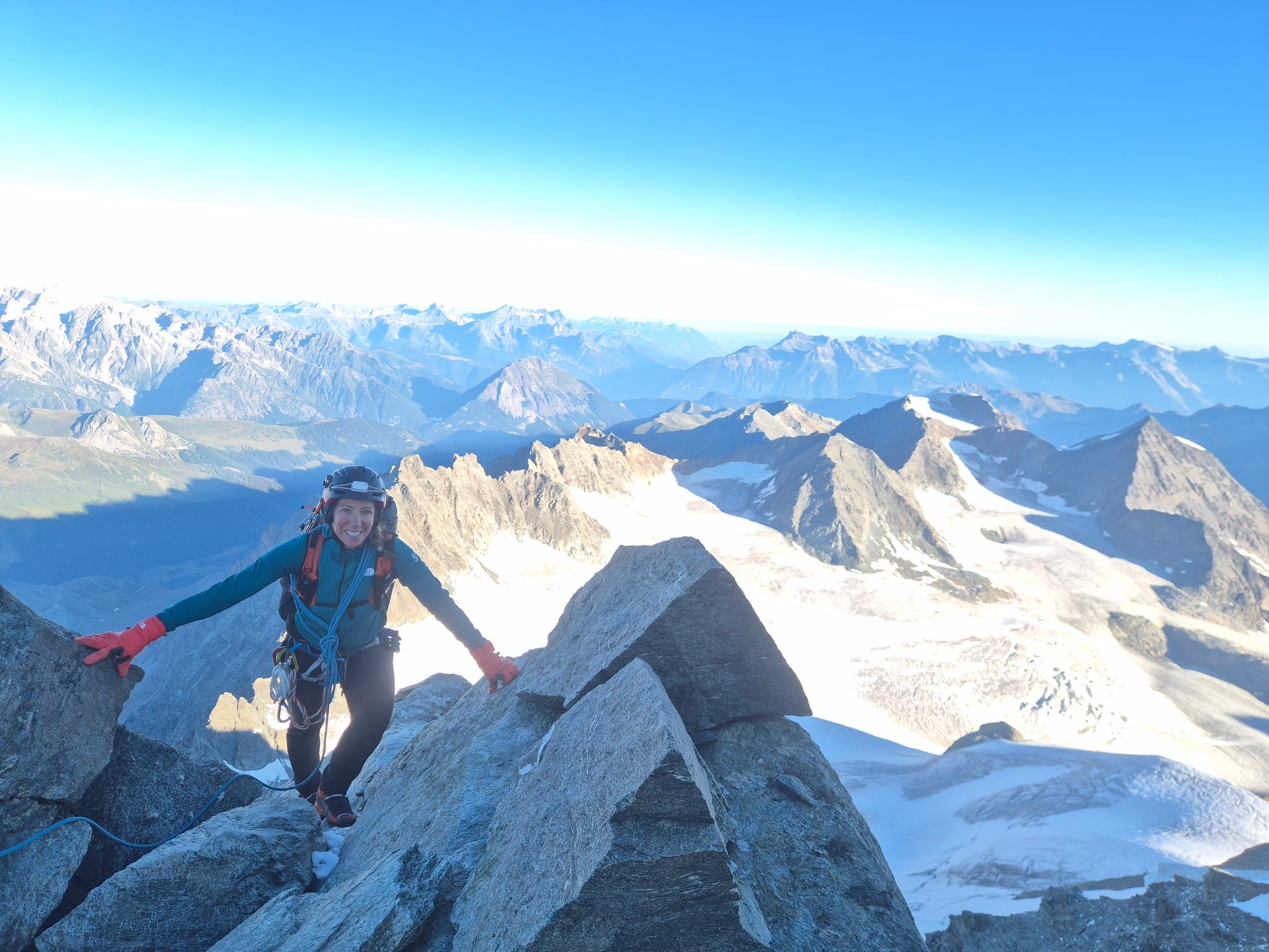 Une alpiniste souriante sur une arête rocheuse du Grand Combin, glaciers et sommets en contrebas