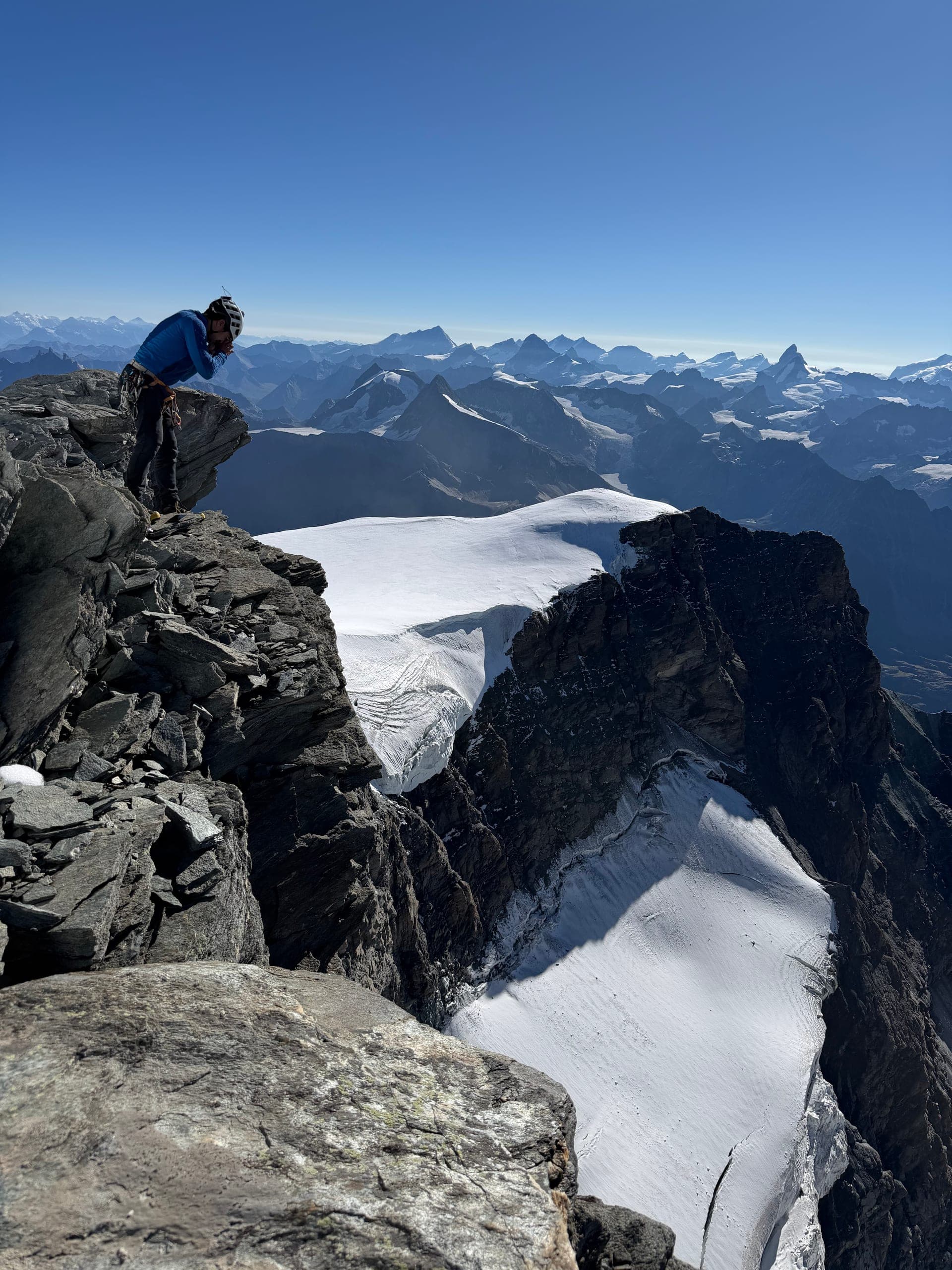 Un alpiniste au bord d’une falaise rocheuse dominant un glacier, sommets au loin