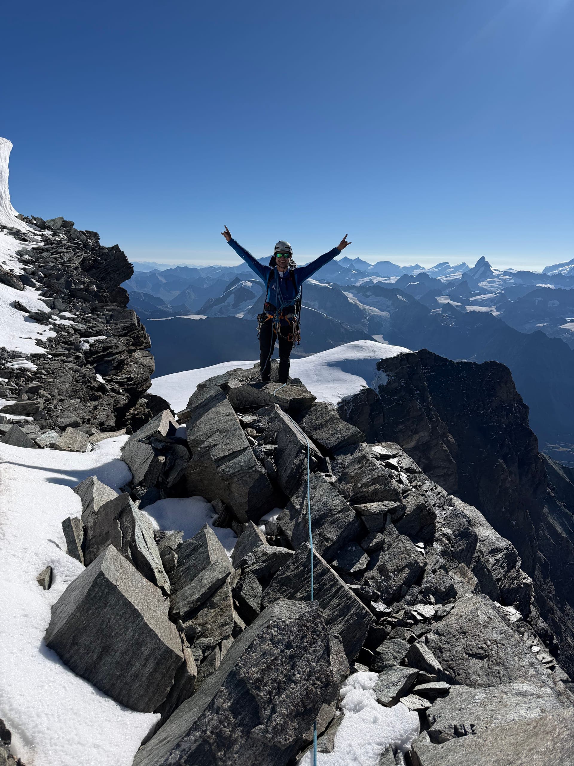 Une alpiniste bras levés sur un sommet rocheux, montagnes à l’horizon