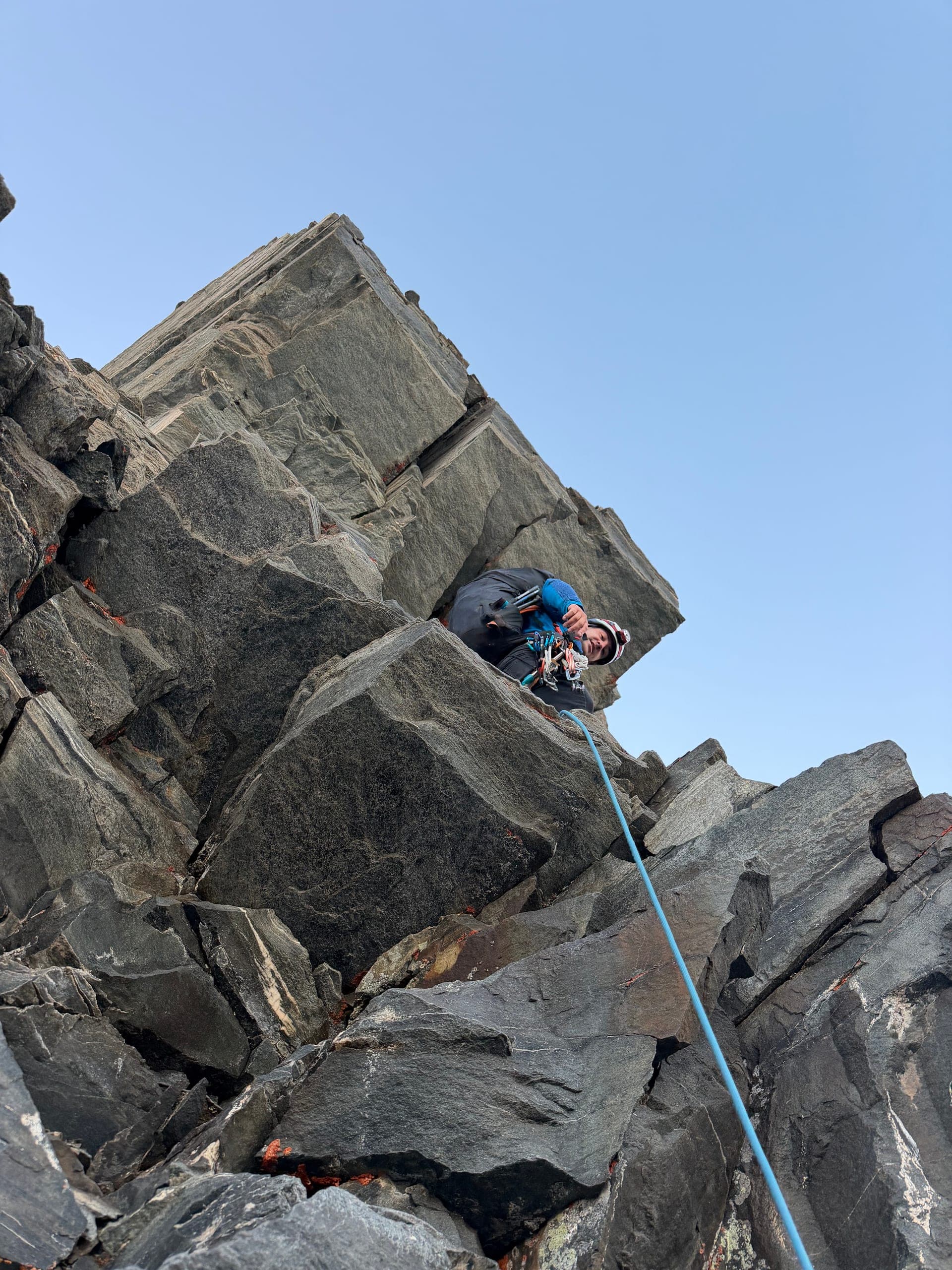 Un alpiniste encordé grimpe dans de gros blocs rocheux sous un ciel bleu