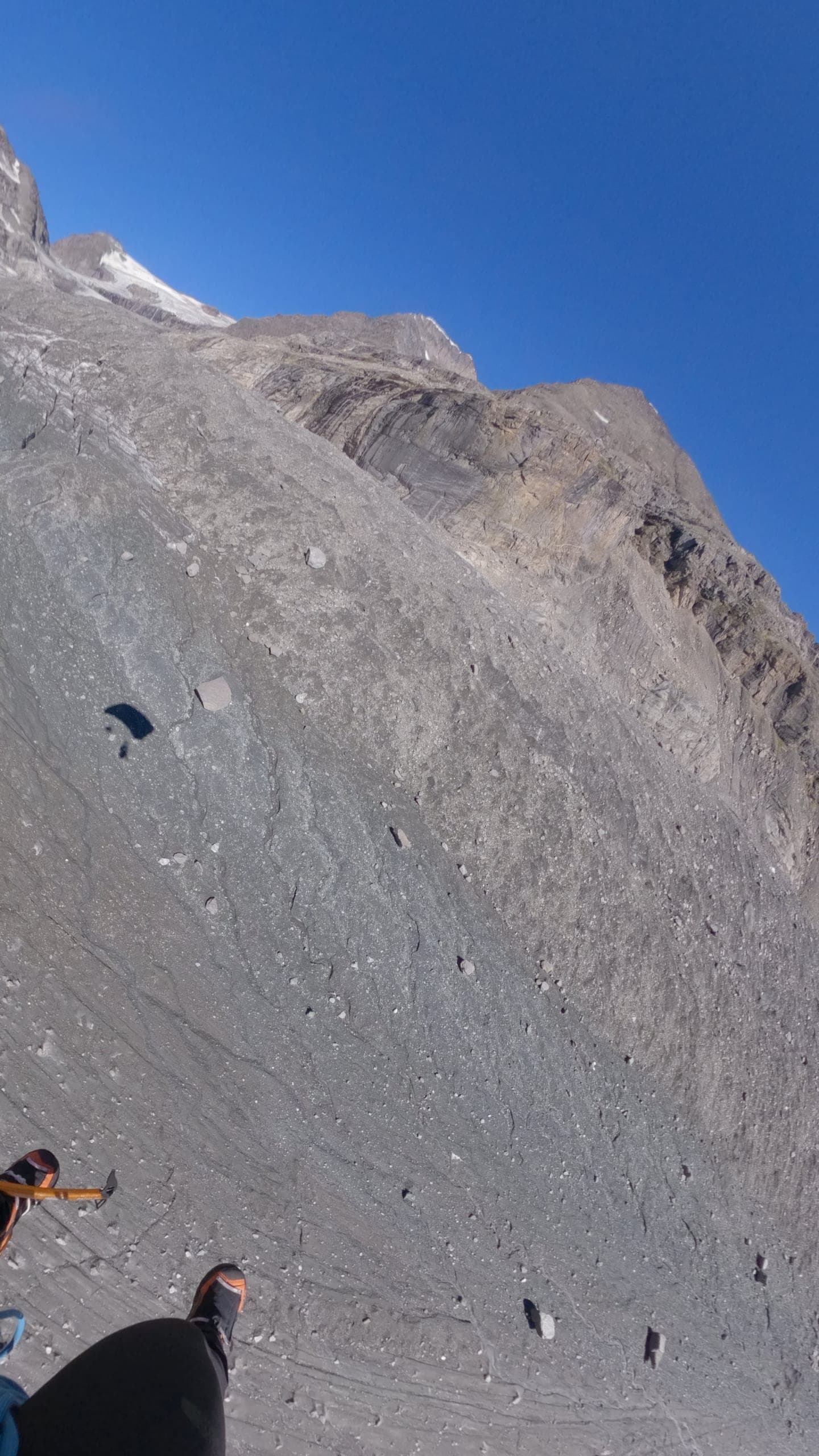 Une wingsuiter en vol le long d’une immense paroi rocheuse grise, ciel bleu en haut