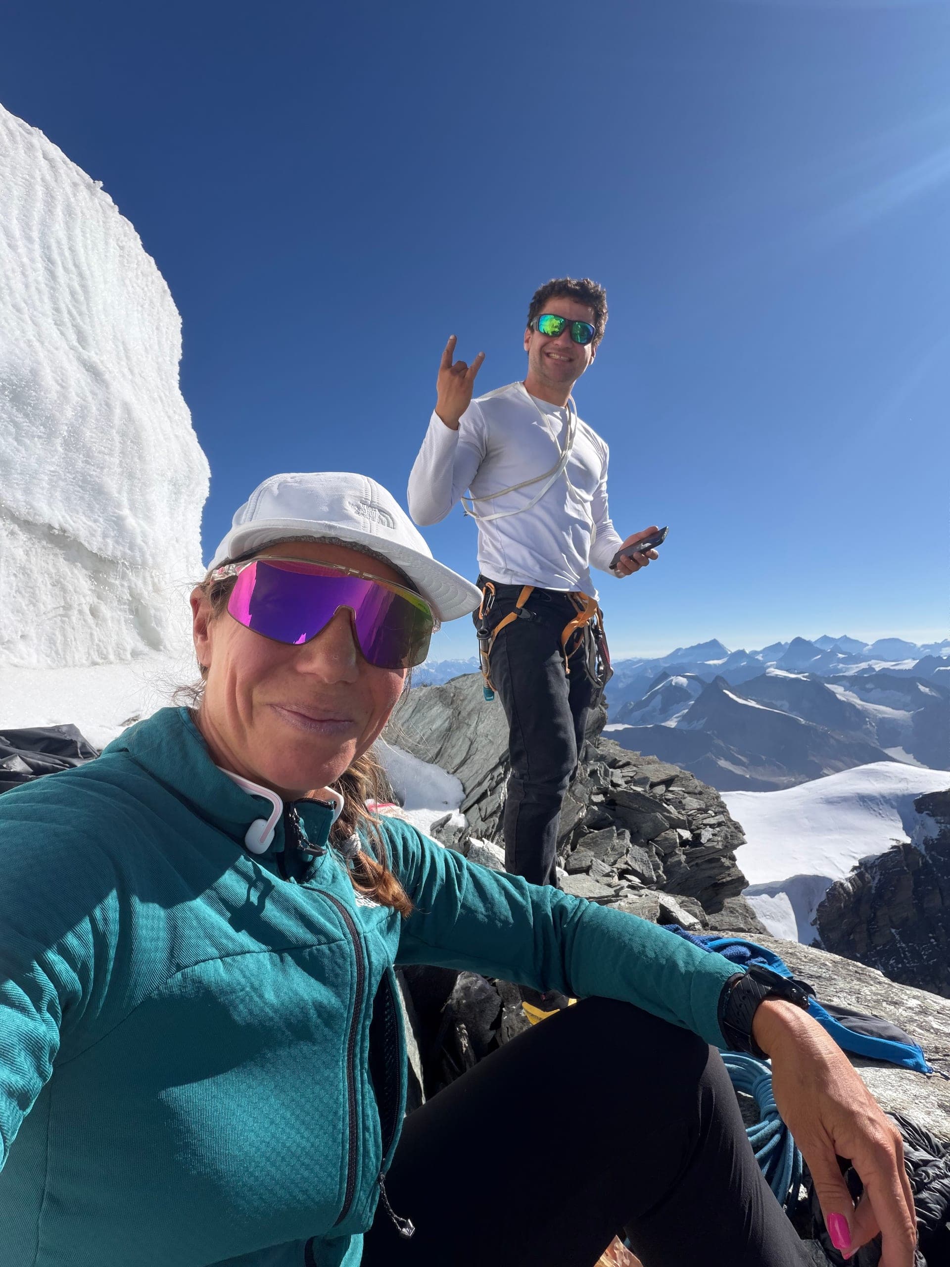 Une alpiniste en selfie près d’un sérac, un homme en chemise claire debout derrière elle
