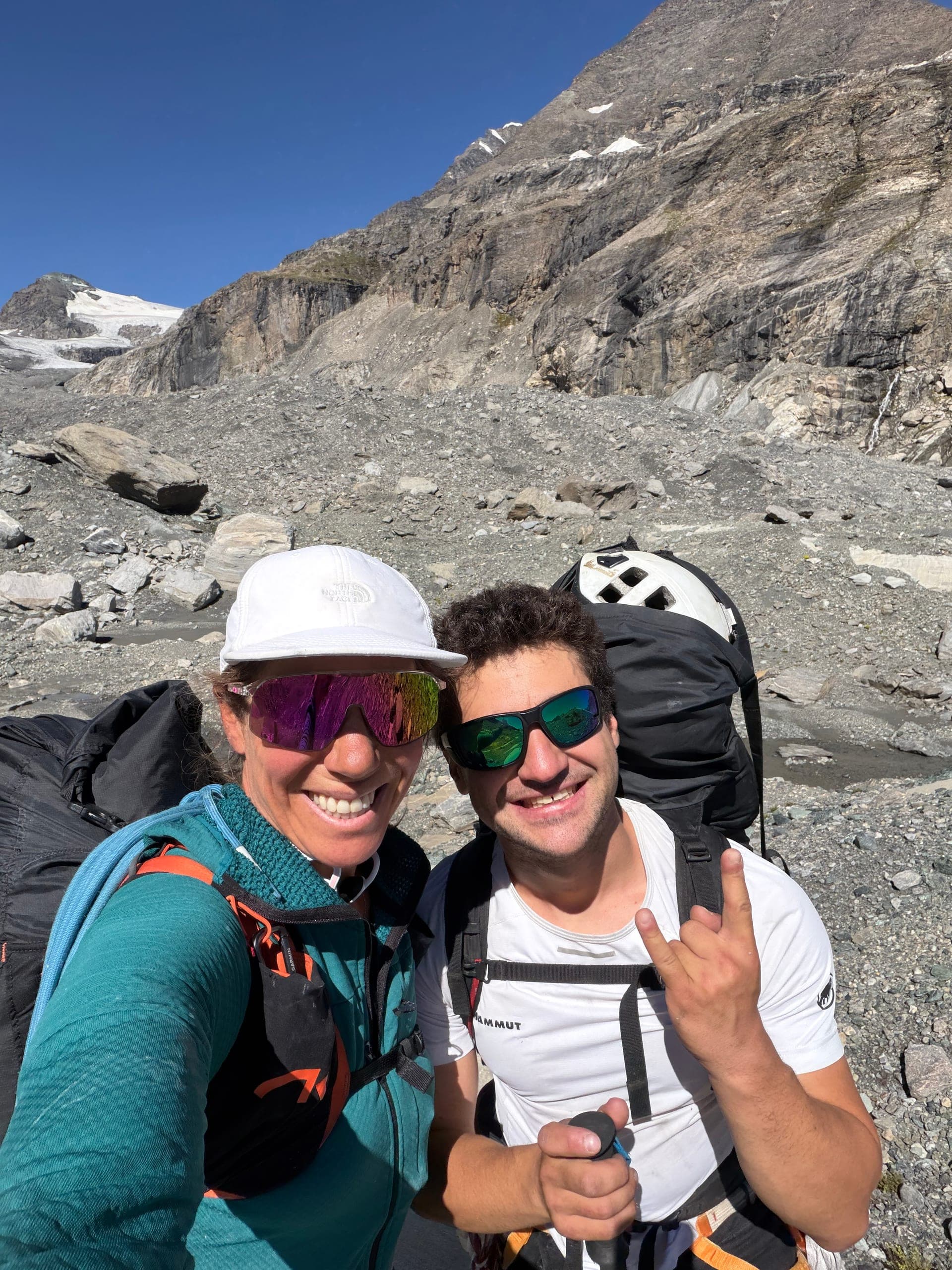 Un alpiniste et une alpiniste en selfie sur des éboulis, geste de la main, après l’atterrissage