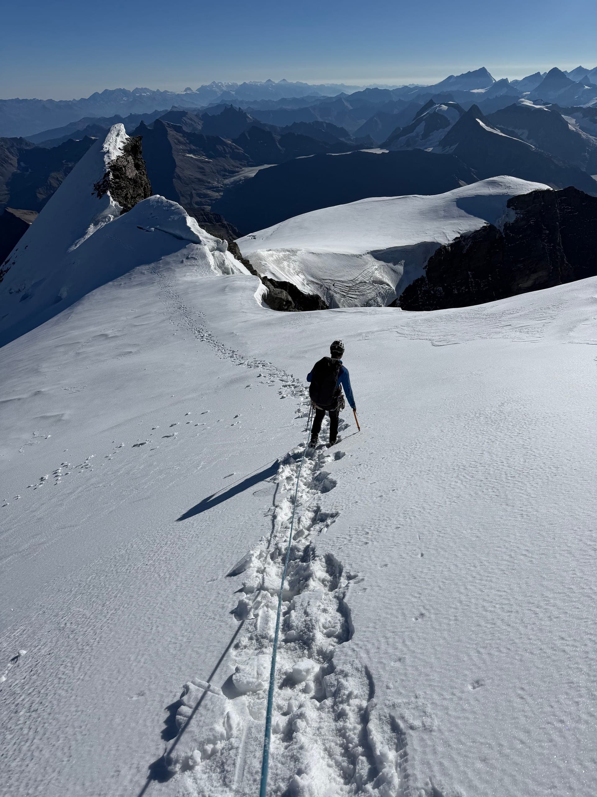 Un alpiniste encordé avance sur une arête de neige, ses traces visibles derrière lui