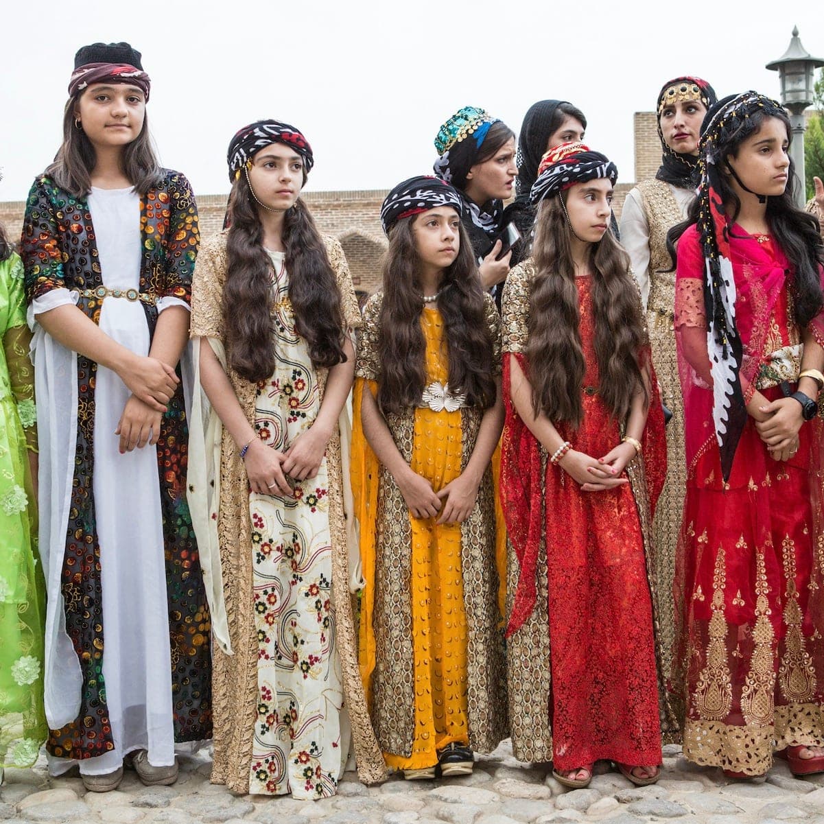 A group of girls in colorful traditional dresses and embroidered headscarves, in Iran