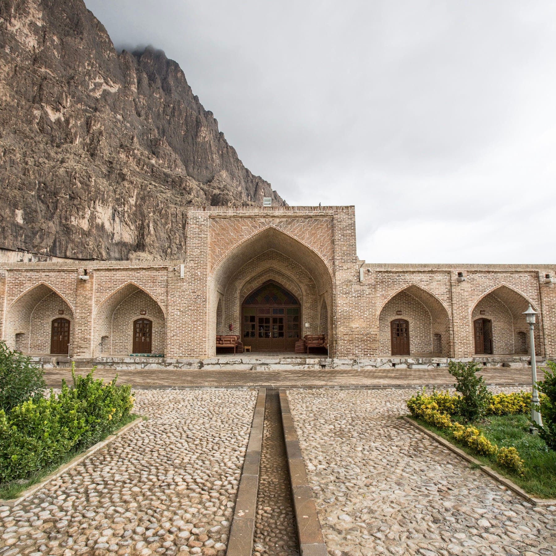 Courtyard of a stone caravanserai with arcades at the foot of a cliff at Bisotoun, Iran