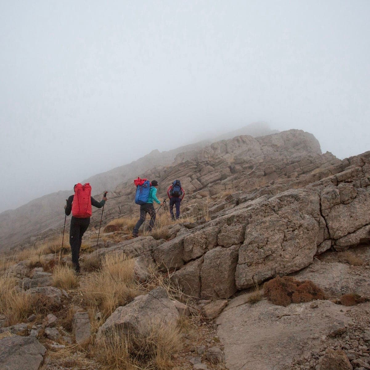 Three hikers in single file on a scree path in fog, Bisotoun
