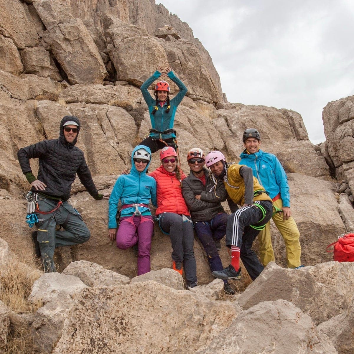 A group of climbers posing on rocks, one with arms raised above the others, Bisotoun