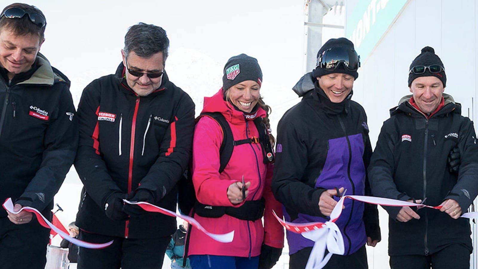 Cinq personnes en tenue de ski coupent un ruban rouge et blanc lors d'une inauguration