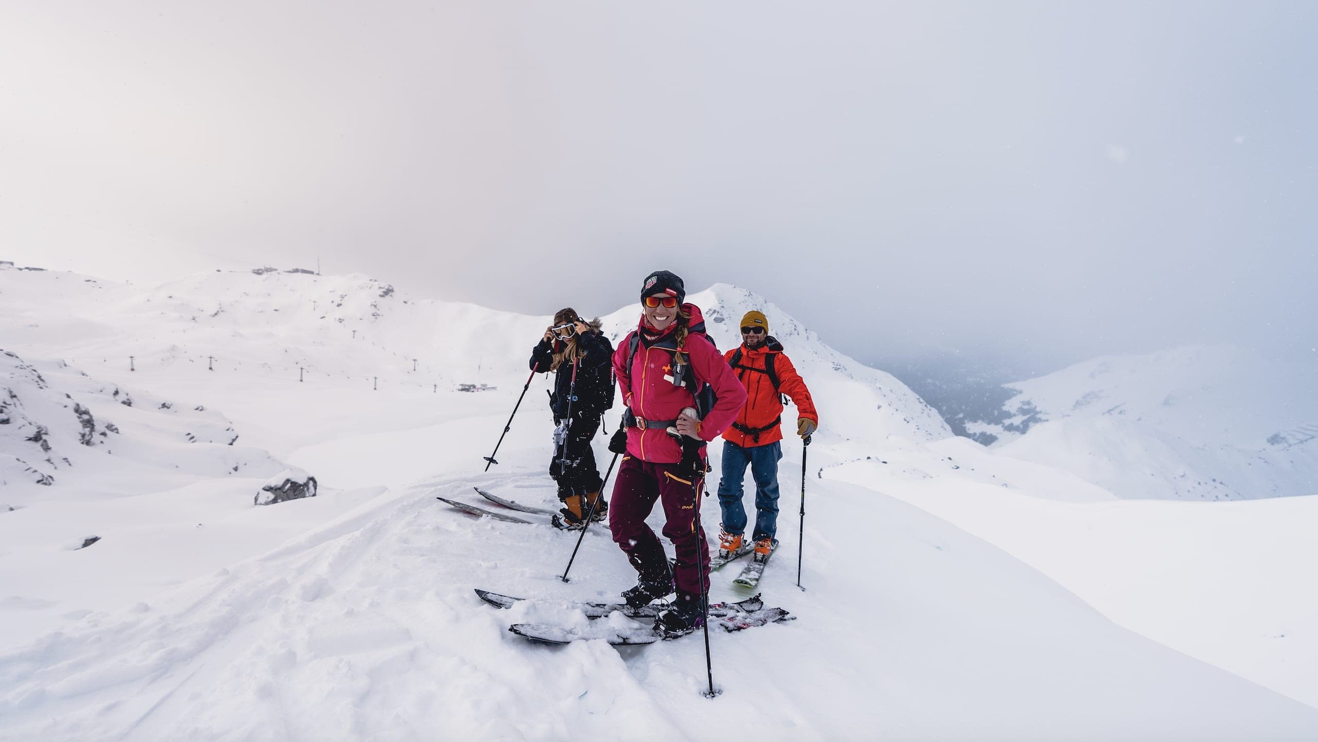 Un petit groupe de skieurs de randonnée pose dans la neige sur un col, skis plantés autour d'eux
