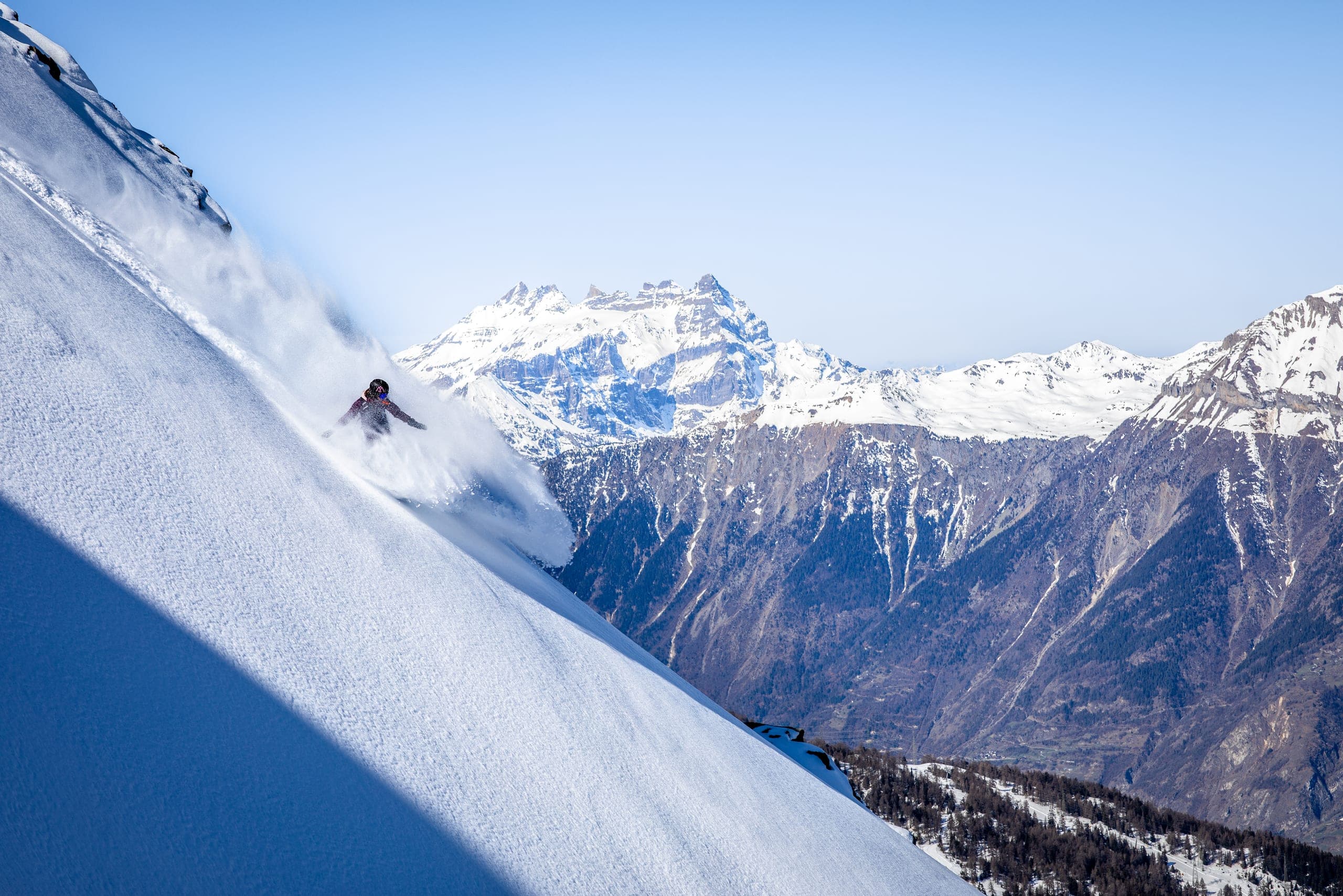 Une snowboardeuse trace sa courbe dans la poudreuse au-dessus d'une vallée et de sommets enneigés