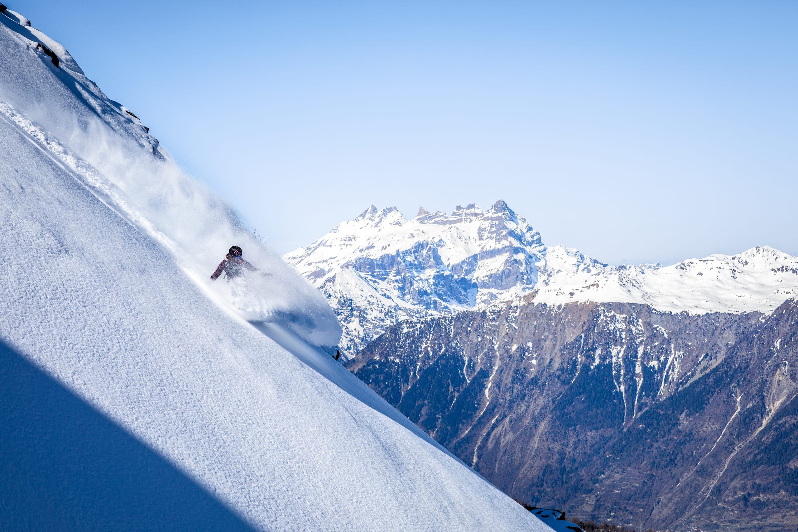 Une snowboardeuse descend une pente de poudreuse, un sommet rocheux enneigé au loin