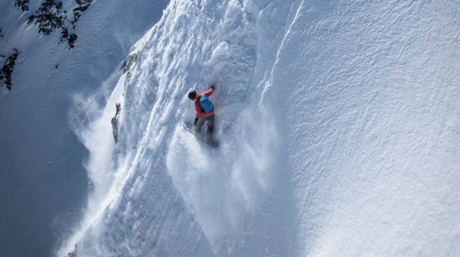 Vue du dessus d'une snowboardeuse dans une pente très raide, la neige giclant derrière elle