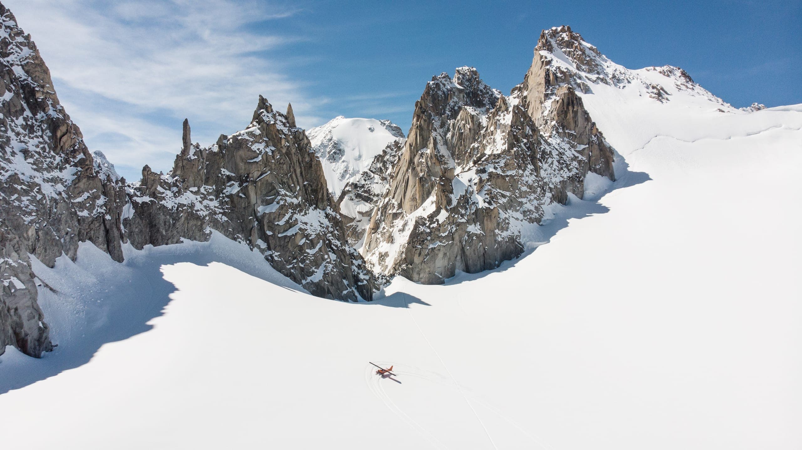 Un petit avion rouge survole un glacier blanc entouré d'aiguilles rocheuses