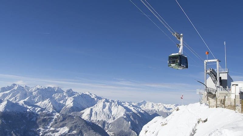 Une cabine de téléphérique suspendue aux câbles près d'une station d'arrivée, face à des montagnes enneigées