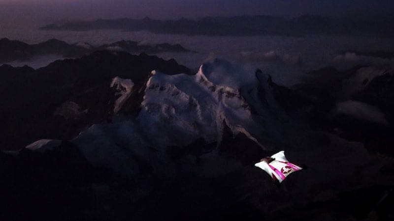 Un pilote de wingsuit rose et blanc en vol de nuit au-dessus d'un massif enneigé dans la pénombre