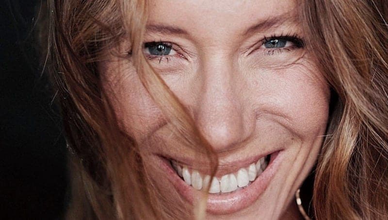 Gros plan du visage souriant d'une femme aux yeux clairs, cheveux dans le vent