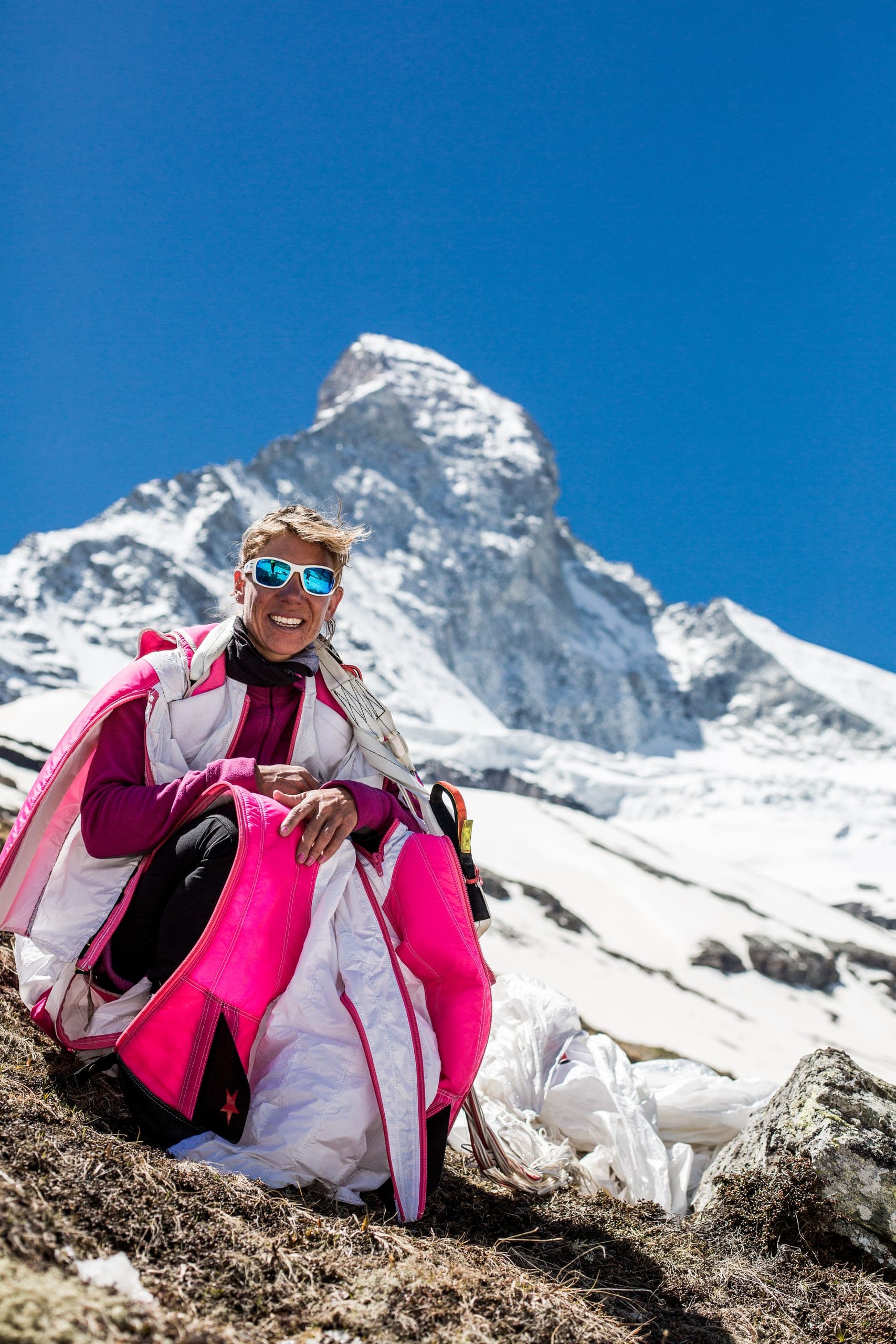 Une pilote de wingsuit accroupie en combinaison rose et blanche, avec le Cervin enneigé derrière elle