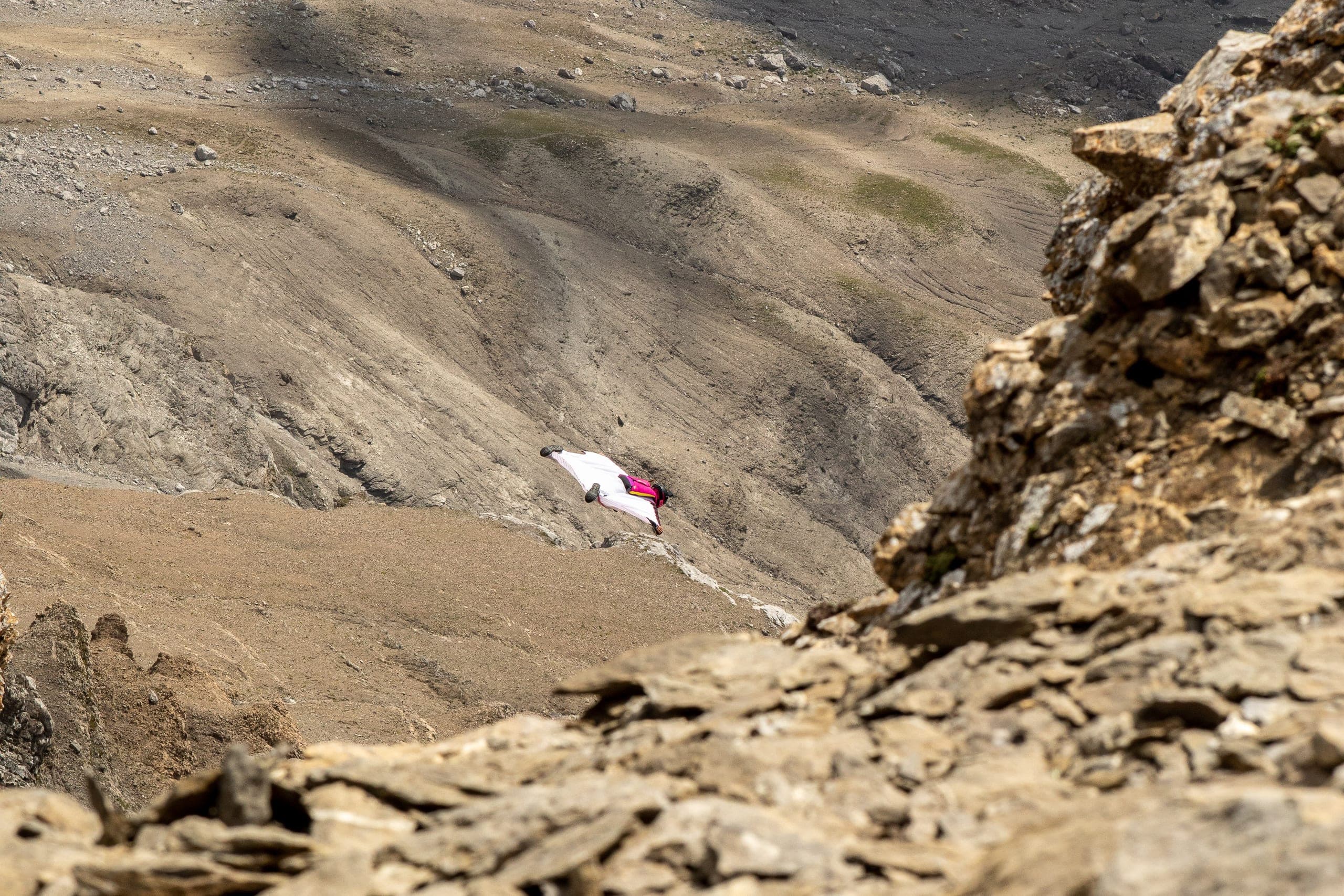 Un pilote de wingsuit survole un versant d'éboulis et de roches, près d'un couloir