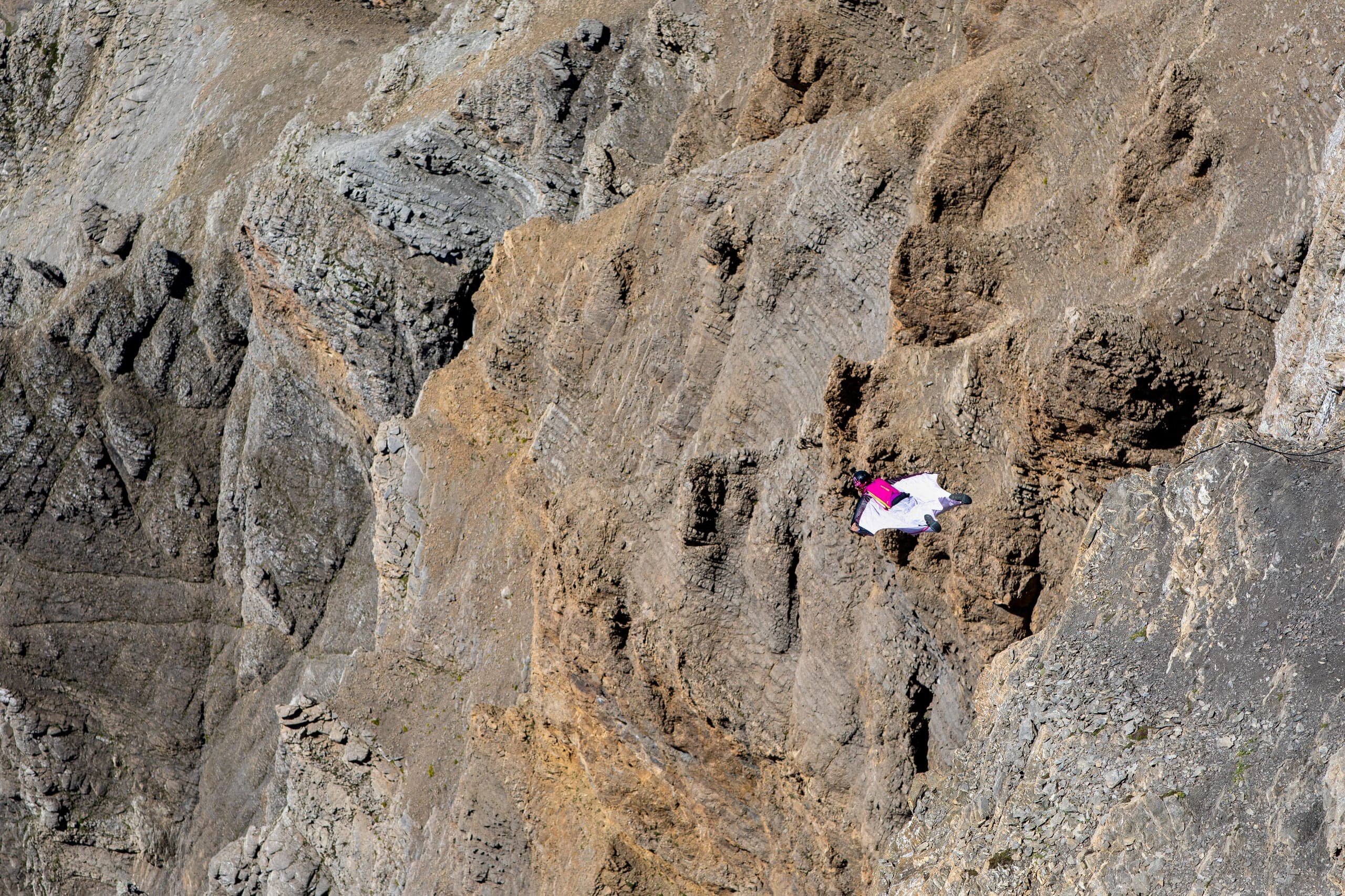 Un pilote de wingsuit blanc et rose vole le long d'une paroi calcaire brun clair