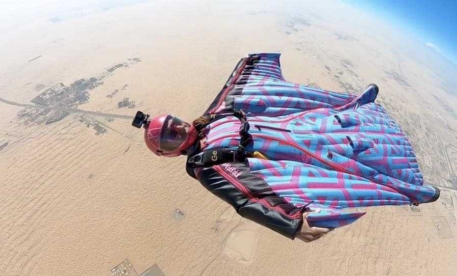 Une pilote de wingsuit à motifs bleus et roses, caméra sur le casque, vole au-dessus d'un désert