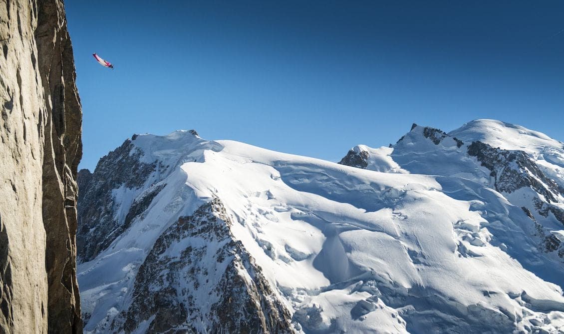 Un pilote de wingsuit passe près d'une paroi rocheuse, face à un grand sommet glaciaire